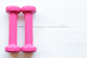 Pink dumbbells for fitness weighing 0.5 kg over a white wooden table