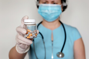 Pills in female hand, physician in medical mask and latex gloves giving transparent bottle of capsules. Concept of dose of drugs, vitamins, coronavirus and flu treatment