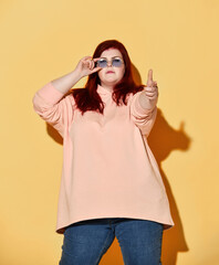 Cool red haired overweight woman in casual clothing points finger at us, gestures finger-gun