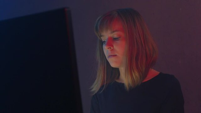 Woman Hacker programmer is working on computer in cyber security center. Monitors light up her face. Neon light flickers in a dark room. Digital resistance.