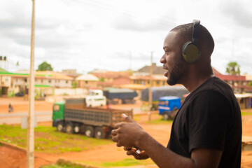 young black man standing outside, using his wireless headphone to listen to songs on his phone