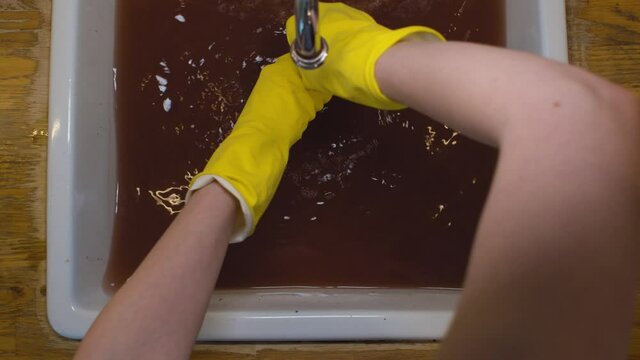 Close up female hands in protective gloves cleaning a blockage in a kitchen sink with a plunger. Reparing of plumbing. Top view