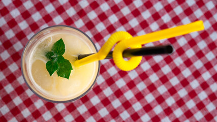 A glass of lemonade on a checkered red-and-white tablecloth. 
