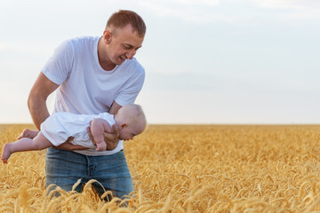 Naklejka na ściany i meble Young father playing with baby. Child flies over field in dads hands. Ripe wheat field.