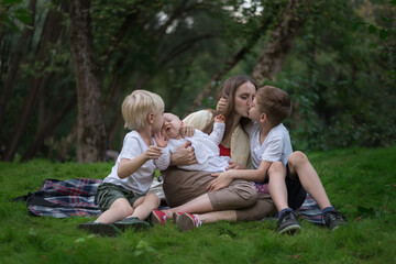 Naklejka na ściany i meble Family picnic at garden outdoors. Mother and three children sitting on picnic blanket in the Park. Mom kisses son