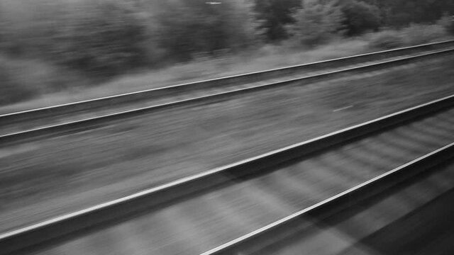 Black and white video footage of railway road tracks in motion as seen through out of moving window of passenger wagon.