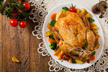 Roast chicken whole. Served on a plate with vegetables and baked potatoes.
