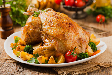 Roast chicken whole. Served on a plate with vegetables and baked potatoes.