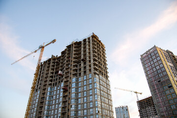 Tower cranes in action during construction residential building on blue sky background. Builder workers during formwork and pouring concrete. Crane lifting a concrete bucket and blocks