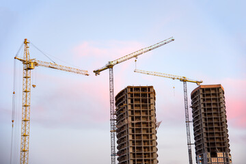 Tower cranes in action at construction site on sunset background. Crane the build the high-rise building. New residential skyscraper. Tall house renovation project, government programs