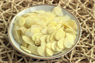 Vintage saucer with thin almond chips on a background of wicker serving napkins. Lifestyle concept, healthy food