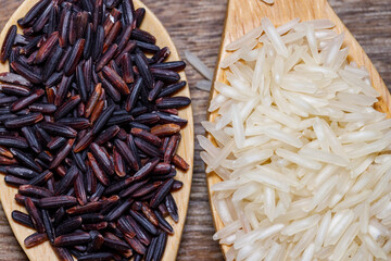 Black wild rice on a wooden spoon, white jasmine rice on a wooden spoon, on wood background. Negative space and copy space. Concept of healthy food.