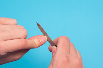 Hand body care. Woman polishes nails with nail file on blue background, close-up, copy space. Business idea, nail salon
