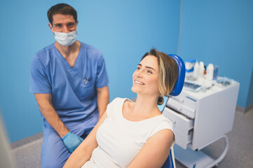 Dentist examining a patient's teeth using dental equipment in dentistry office. Stomatology and health care concept. Young handsome male doctor in disposable medical facial mask, smiling happy woman.