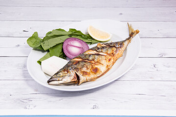 lemon and onion with grilled fish next to it on a white wooden background