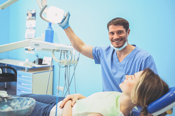 Obraz premium Dentist examining a patient's teeth using dental equipment in dentistry office. Stomatology and health care concept. Young handsome male doctor in disposable medical facial mask, smiling happy woman.