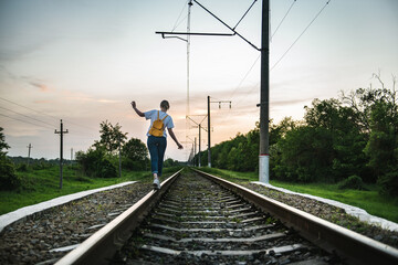 girl goes by rail among the forest on a sunset background