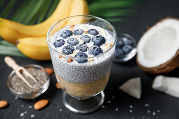 Chia seeds pudding with banana puree and blueberries in glass.