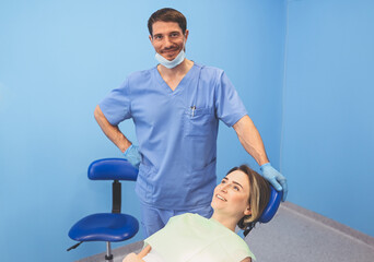 Dentist examining a patient's teeth using dental equipment in dentistry office. Stomatology and health care concept. Young handsome male doctor in disposable medical facial mask, smiling happy woman.