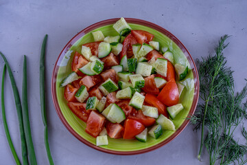 Plate of vegetable salad surrounded by fresh green onion and dill on concrete background
