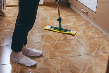 A woman washes the floor of tiles in the kitchen with a mop. Cleaning of the apartment. yellow rag. cleaning house cleaning. we kill microbes