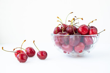Ripe cherry berries with sprigs in a glass plate on a white background. The concept of a healthy diet and vegetarianism.