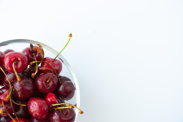 Ripe cherry berries with sprigs in a glass plate on a white background located on the left edge of the image. Top view. The concept of a healthy diet and vegetarianism. Close-up.