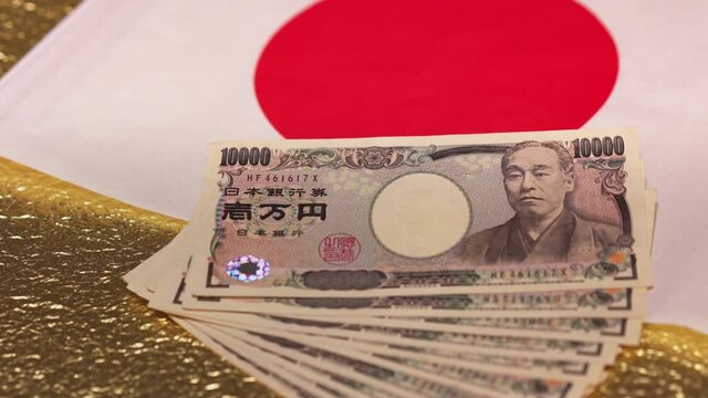 tokyo, japan - may 26 2020: Slide video of 100,000 yen in cash sent by Japanese govt of Abe Shinzo to fight economic unemployment caused by COVID-19 on a Japan national flag and golden background.