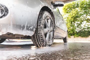 the car is covered with foam at a self-service car wash. Close-up of front bumper and wheel