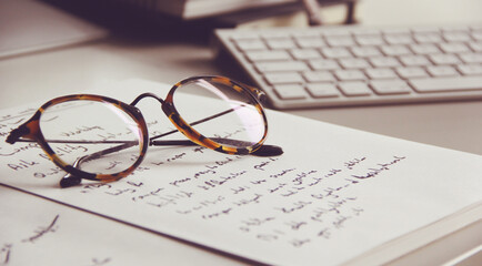 old vintage reading glasses on white note paper with keyboard background