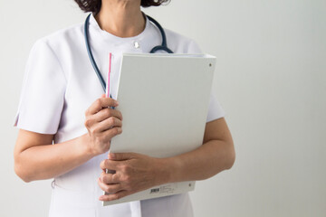 A nurse woman wearing medical coat with a stethoscope write test results in the hospital sheet chart. Serious excited for success medical worker posing on light background