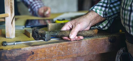 Detail of carpenter's hand holding a hammer leaning on the workbench