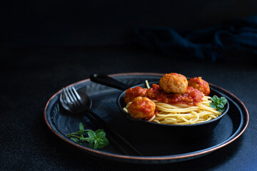 Italian spaghetti pasta with meat balls and tomato sauce served with oregano in a pan on a dark table and black background. Close-up, copy space