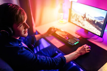 gamer playing computer games online with headphones, in a room with neon light.