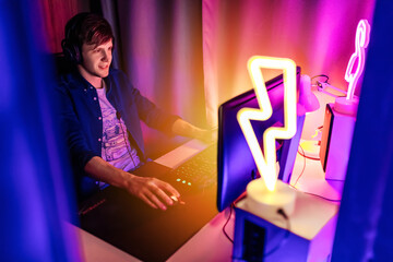 gamer playing video games on a computer with headphones and using a colorful backlit keyboard
