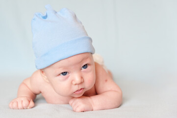 A smiling baby with blue eyes smiles and crawls on a blue sheet.