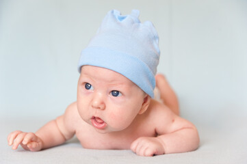 A smiling baby with blue eyes smiles and crawls on a blue sheet.