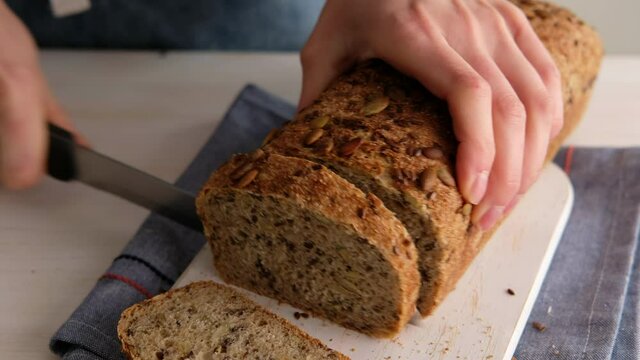 Woman hands close-up slices bread from whole wheat flour, flax, sunflower and pumpkin seeds close-up on a wooden background. Wholemeal Bread.