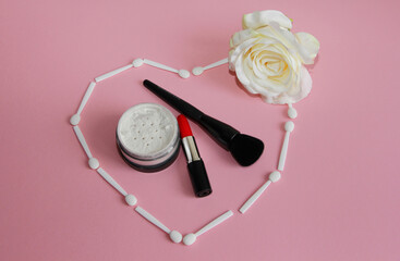 Obraz na płótnie Canvas red lipstick, powder and makeup brush in a heart of white shadow applicators and a rose on a pink background