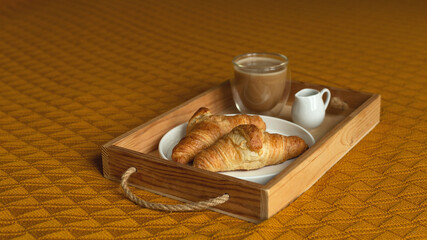 Homemade croissants and coffee on a wooden tray.