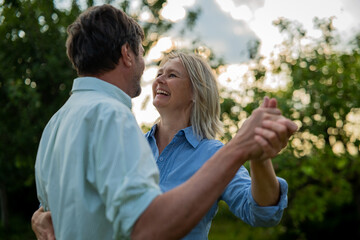 Authentic shot of lovely happy mature couple is enjoying time together and having fun dancing to celebrate their timeless love on a background of a green nature.