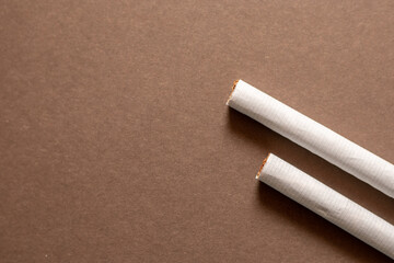 Two cigarette end laying flat on a brown background. Left area empty for copyspace