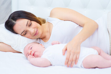 A newborn baby lies in front of mom on a large parental bed. Mom stroking her baby's tummy