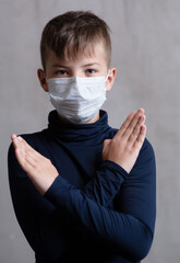 A boy in a medical mask put forward crossed arms symbolizing a stop.