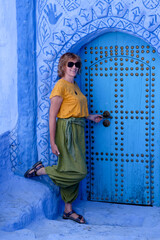 Pretty smiling woman standing near painted door in the blue city of Chefchaouen, Morocco.