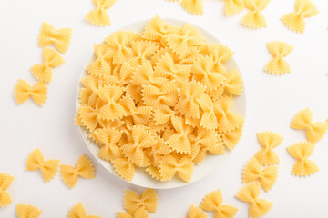 Dried Farfalle Rigate Italian pasta in a round bowl ready to be cooked, isolated on a white table, top view or flat lay of healthy food 
