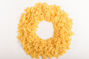 Heap of dried Farfalle Rigate Italian pasta ready to be cooked, isolated on a white table, top view or flat lay of healthy food displayed as a circle
