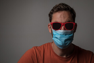 New normal caucasian man wearing a covid coronavirus protective mask and red sunglasses. Cool male with sunshades and face mask.