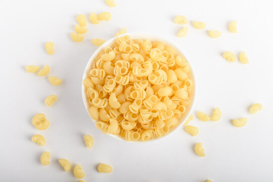 Dried cornetti rigati Italian pasta in a round bowl ready to be cooked, isolated on a white table, top view or flat lay of healthy food 
