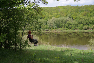 Obraz na płótnie Canvas Woman swings on a rope swing on the Oka riverbank. Spring green scenery, near Tarusa, Russia.